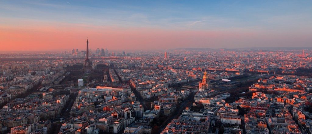 Aerial shot of Paris featuring the Eiffel Tower taken at dusk with vibrant pink and blue hues