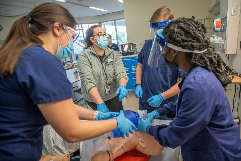 Students dressed in navy scrubs receiving instruction on performing CPR in a School of Nursing Simulation Lab.
